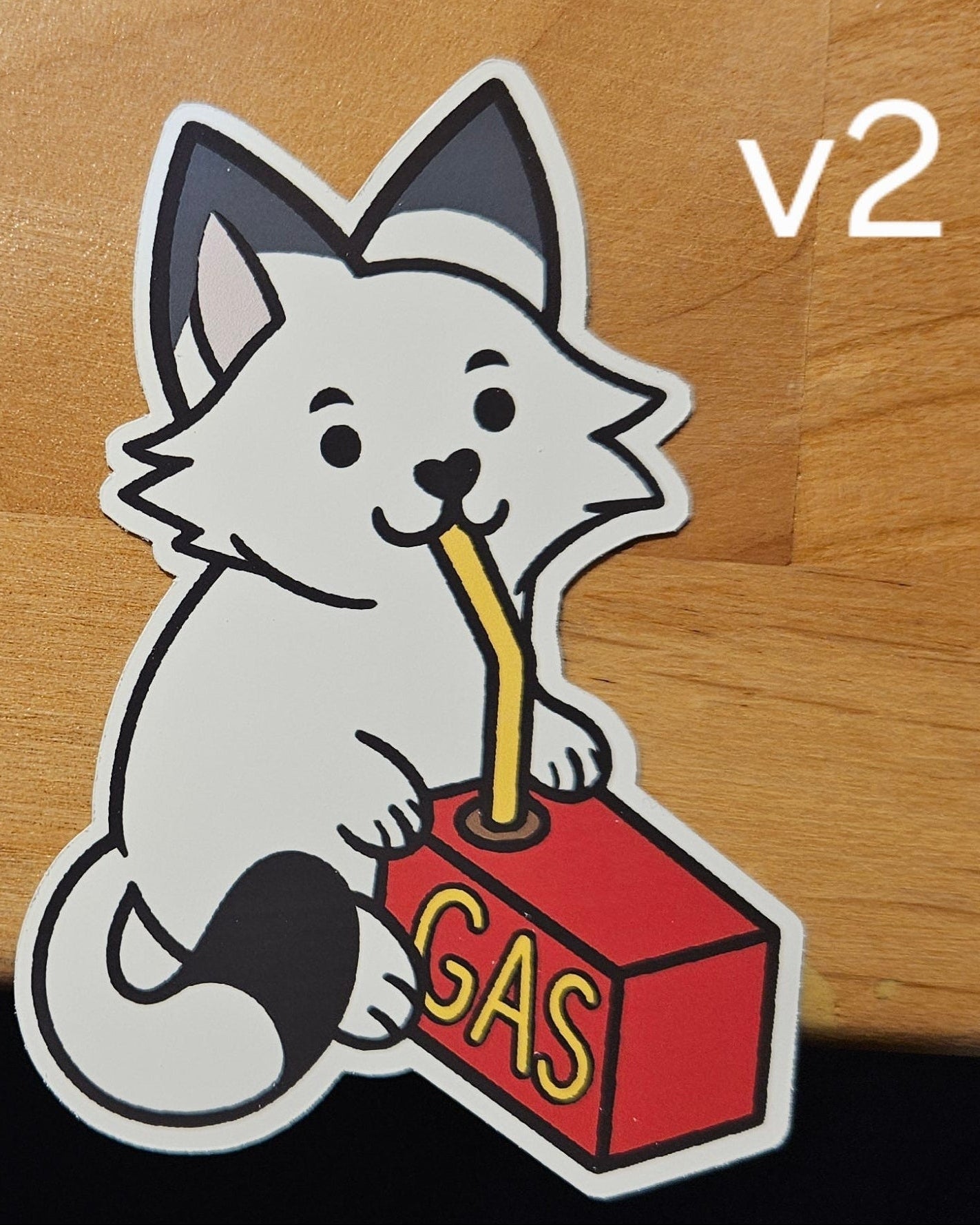 sticker labeled 'v2' featuring a furry creature drinking from a a gas canister on a wooden surface.